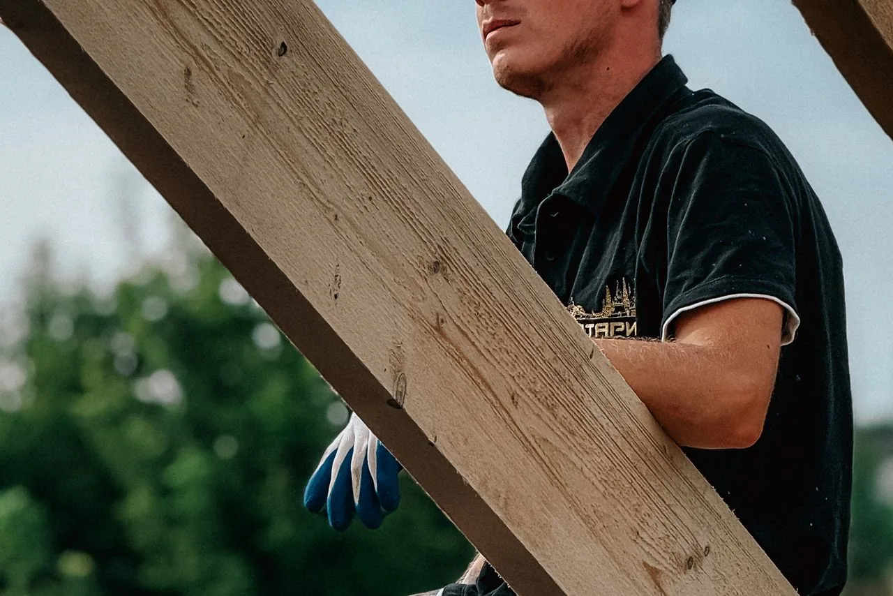 Un charpentier porte une pièce de bois sur un chantier